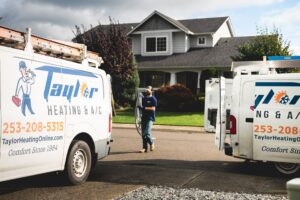 Two Taylor Heating & A/C service vans parked in a residential driveway with a technician standing between them near a two-story house.