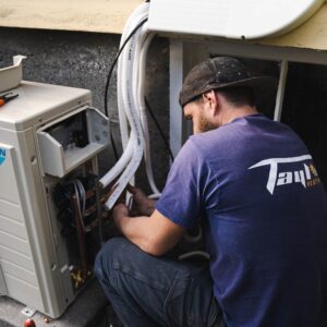 Technician in blue shirt working on white heating unit installation in RV. Professional performing equipment setup and connection.