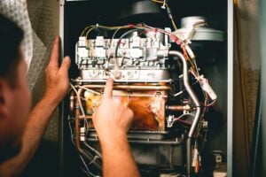 Technician pointing to internal components of an open furnace showing white switches, colored wiring, and copper heating elements.