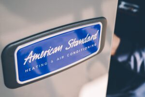 Close-up of a blue and white American Standard Heating & Air Conditioning badge mounted on a vehicle exterior.