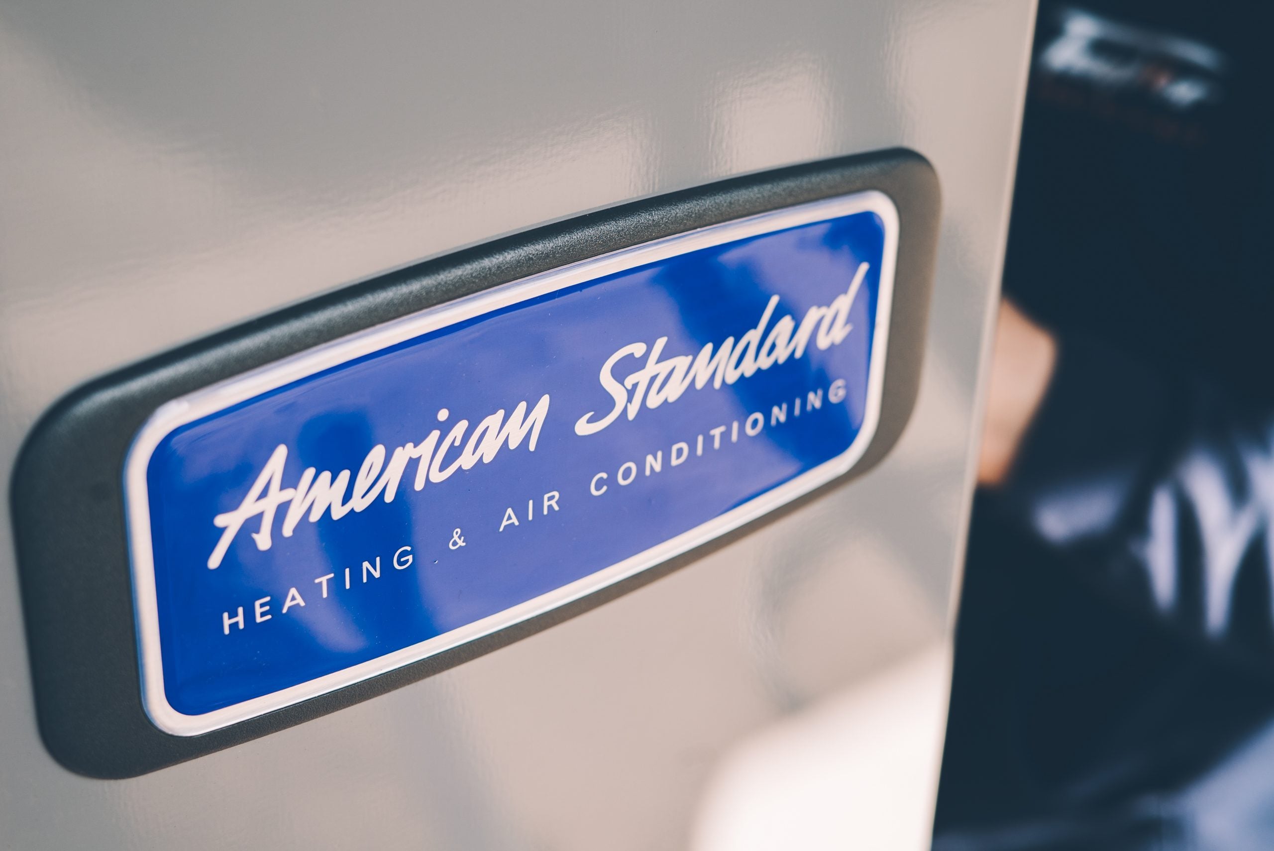 Close-up of a blue and white American Standard Heating & Air Conditioning badge mounted on a vehicle exterior.