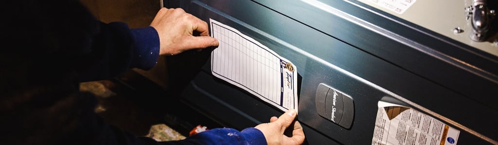 Person's hands examining a white pleated furnace air filter installed in a dark heating unit.