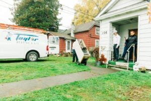 Taylor Heating & A/C service van parked at residential home with technicians meeting homeowners at the front door.