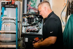 Technician in black Nike shirt examines open boiler unit with Milwaukee tool, revealing internal circuits and wiring connections.