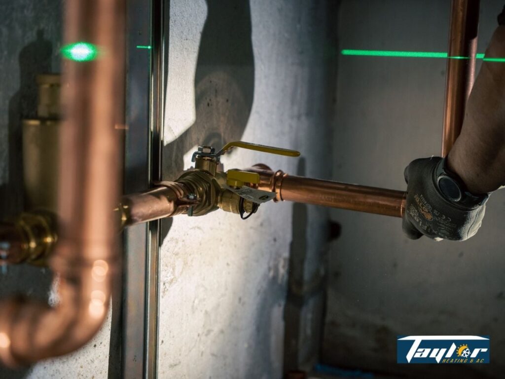 Green laser level beam aligned horizontally across copper pipes and plumbing fixtures on a concrete wall.