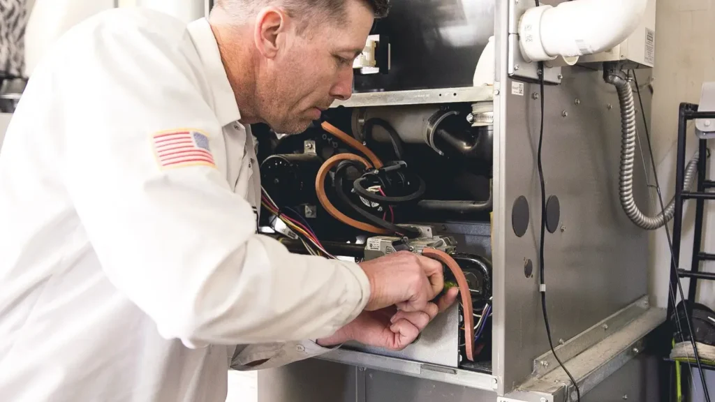 Technician in white uniform with American flag patch inspecting internal components of a furnace system.