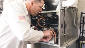 Technician in white uniform with American flag patch inspecting internal components of a furnace system.