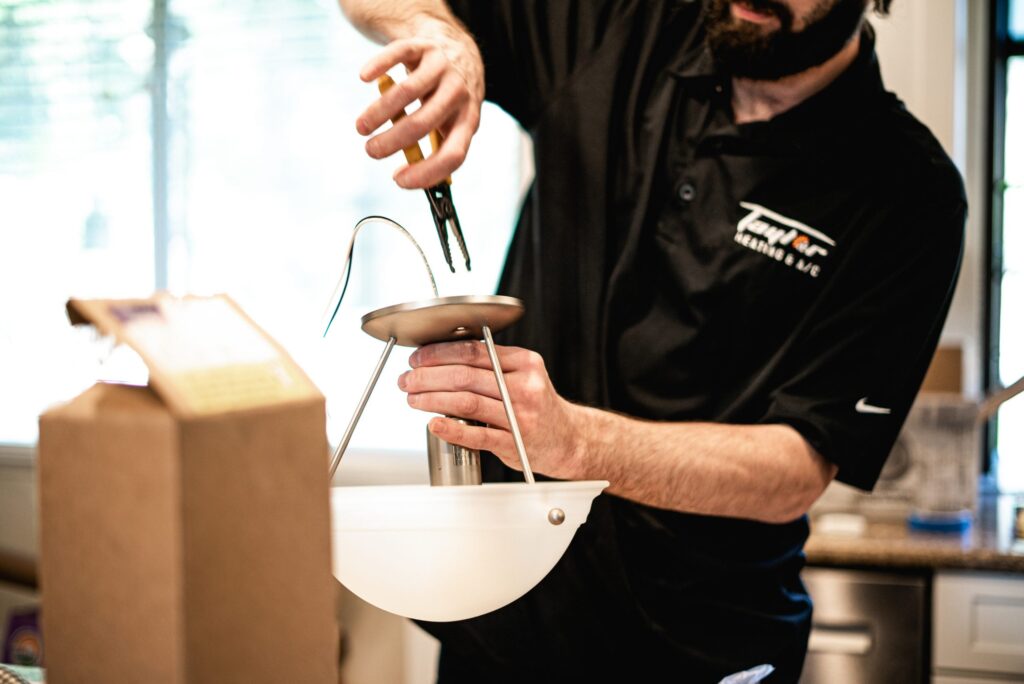 Chef in black shirt using tongs to strain pasta from a white colander over a pot in a kitchen.