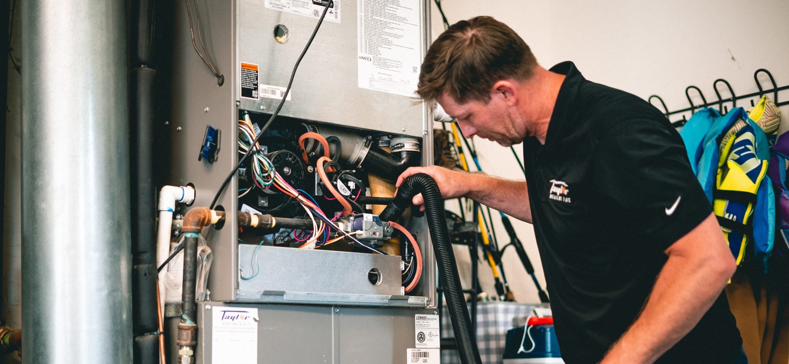 Technician in black shirt inspecting internal components of residential furnace with wiring and motor visible.