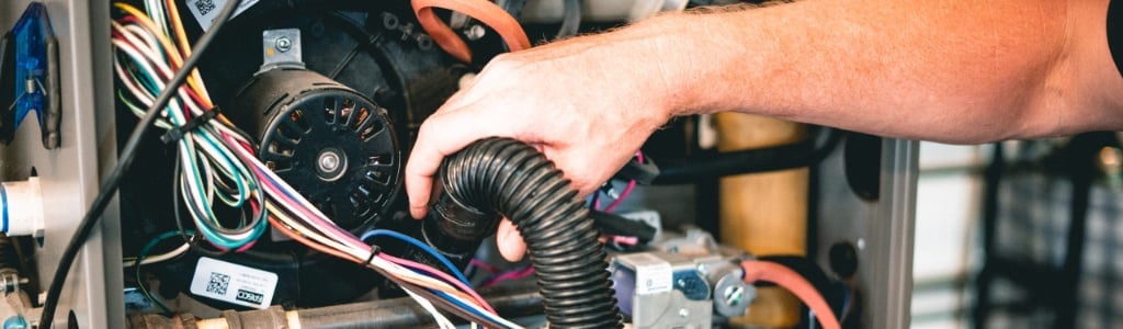 Technician's hand adjusting flexible ductwork connected to a furnace blower motor with visible wiring and electrical components.